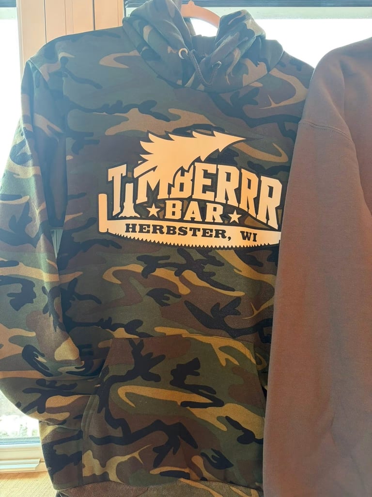 Timberrr Bar hoodie with camouflage pattern and yellow logo, hanging indoors