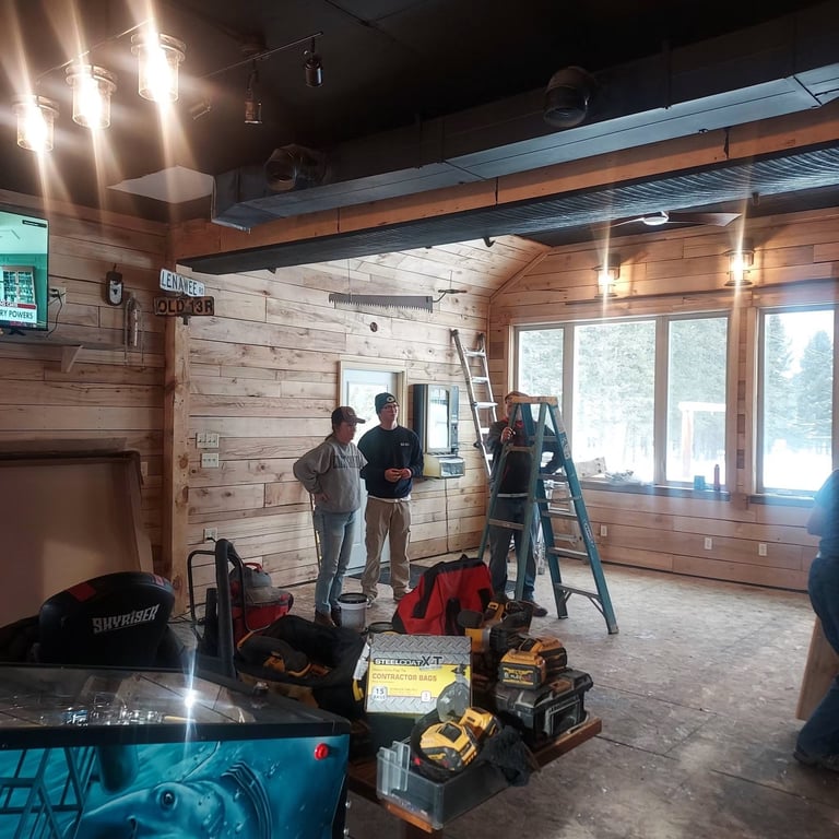 Workers installing drywall in a wood-framed interior with construction tools and equipment on the floor.