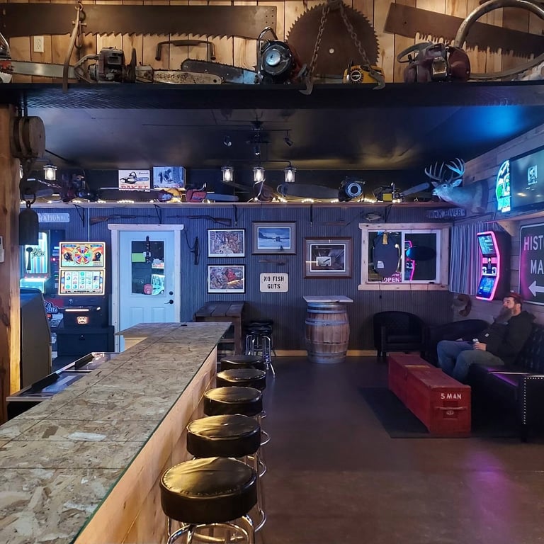 Man cave workshop with bar counter, neon signs, arcade games, and vintage industrial equipment on shelves