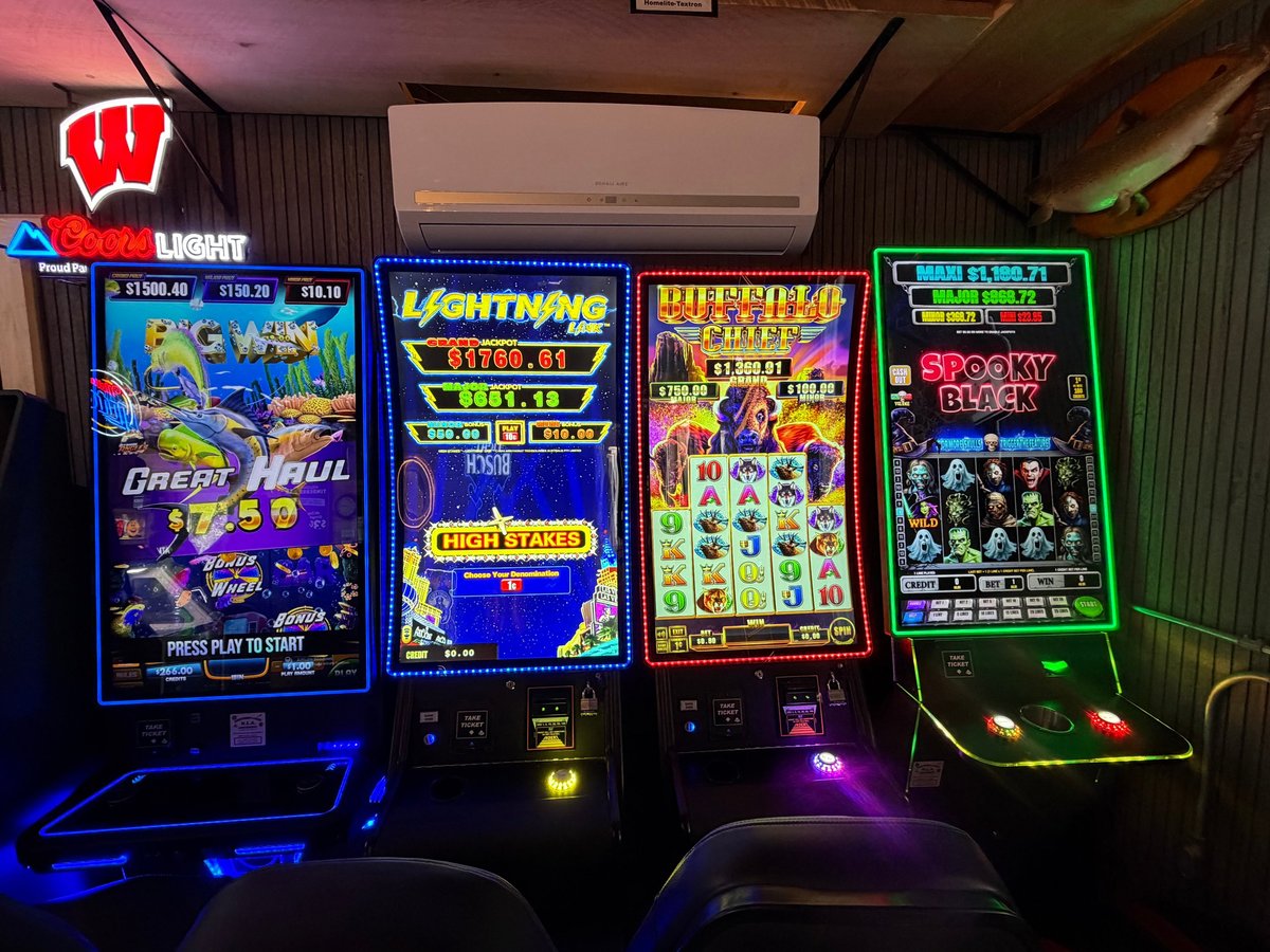 Row of illuminated slot machines including Great Haul, Lightning Link, Buffalo Chief, and Spooky Black glowing blue at the Timberrr Bar