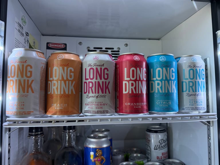 Six colorful Finnish Long Drink cans — Peach, Zero Sugar Peach, Raspberry, Cranberry, Traditional Citrus, and Zero Sugar Citrus — arranged on a refrigerator shelf