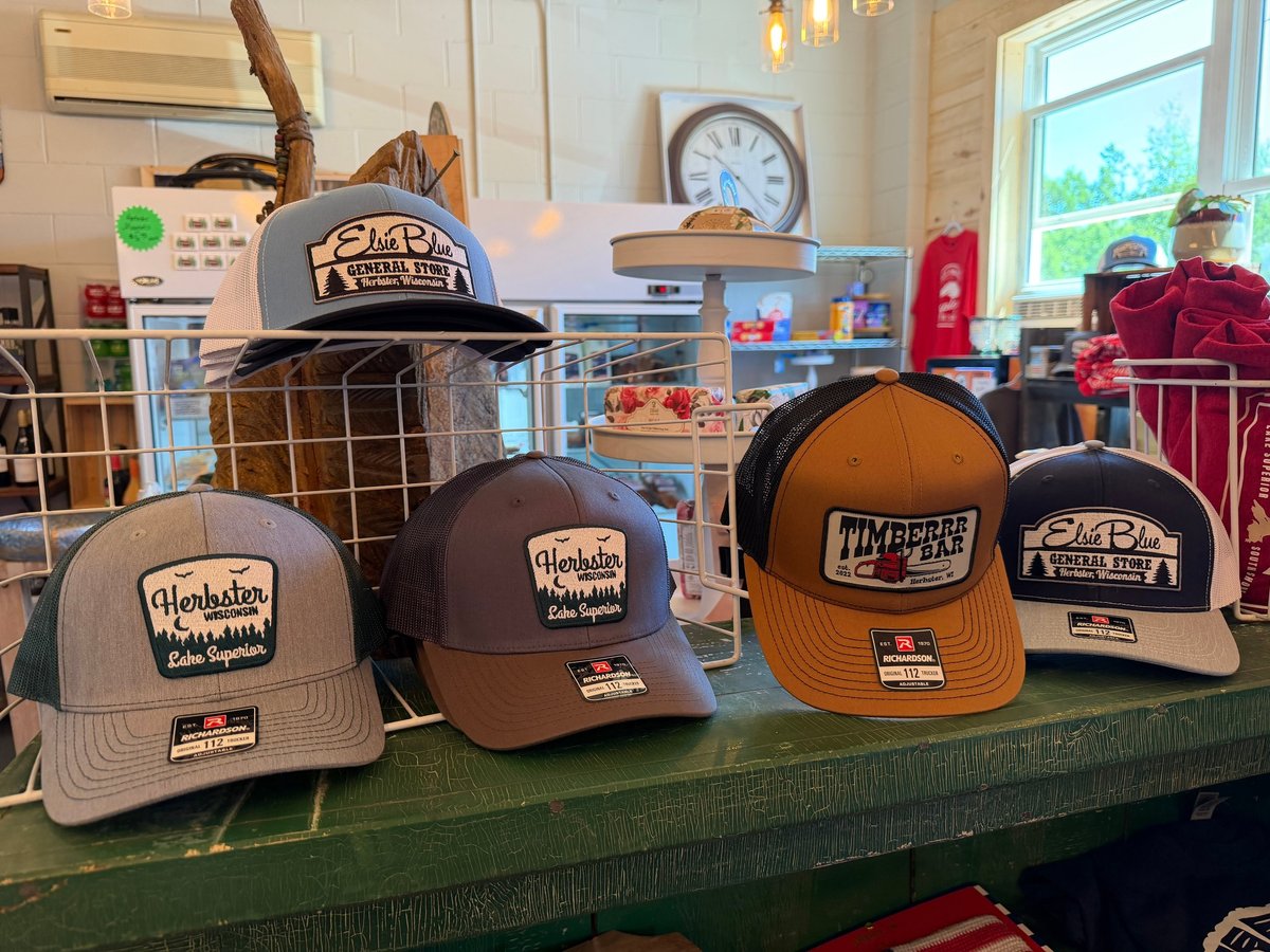 Display of branded trucker hats featuring Elsie Blue General Store, Timberrr Bar, and Herbster Wisconsin logos