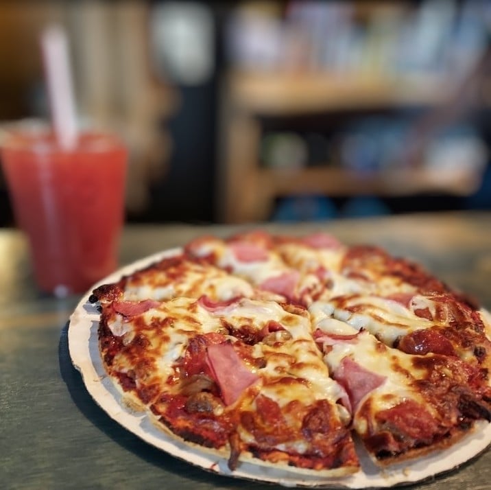 Sliced pizza with ham and pineapple on a white plate, with a red beverage in the background