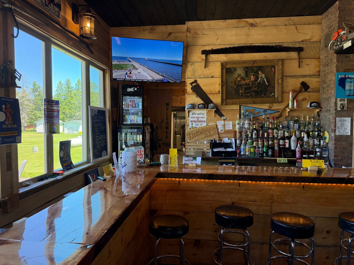 Wooden bar counter with brown leather stools, shelves of liquor bottles, big windows looking out over trees and Lake Superior in the distance