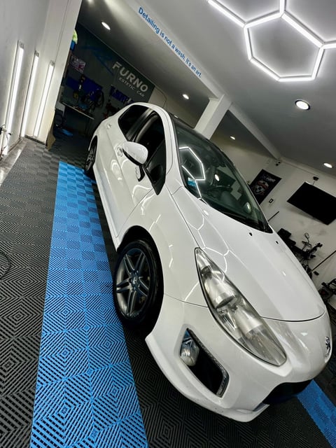 White compact car displayed in a modern showroom with blue flooring and geometric ceiling lights