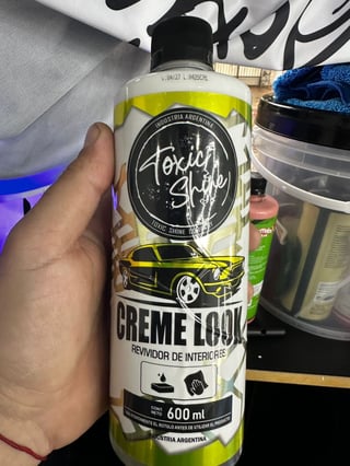 Hand holding a Toxita Shop Creme Loom car interior cleaner bottle with yellow-green label and black car graphic