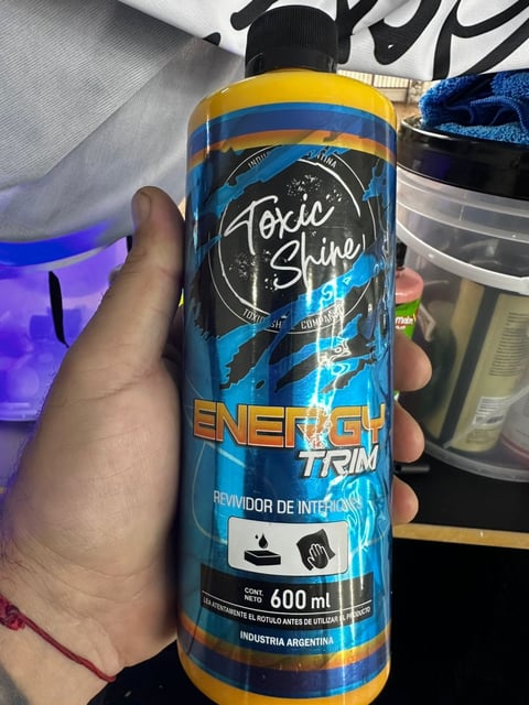 Person holding a blue and yellow bottle of Toxic Shine Energy Trim car detailing product, 600ml size
