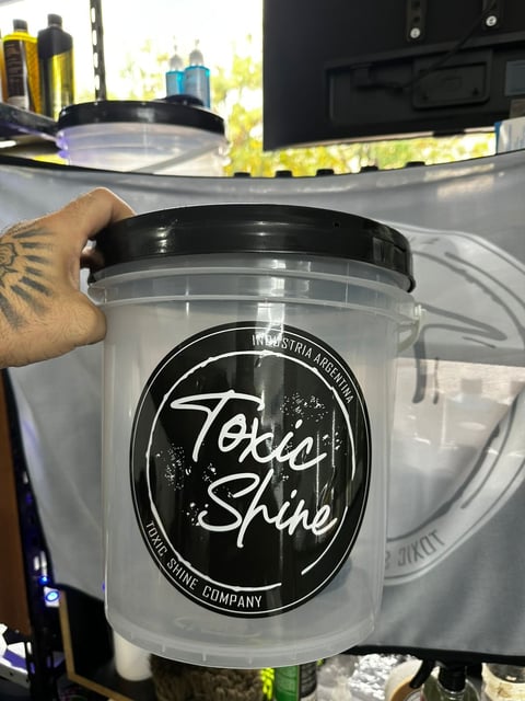 Person holding a clear plastic container labeled Toxic Shine with black lid, product display at salon or retail shop