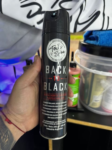 Person holding a black aerosol spray can labeled Back in Black with product information and a circular logo on the label
