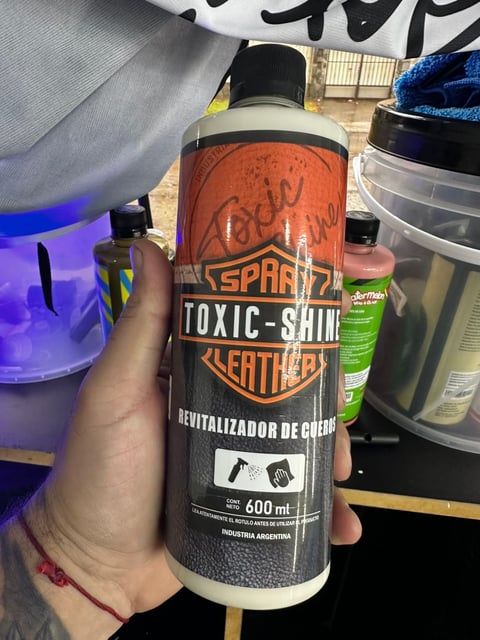 Hand holding a bottle of Toxic Shine leather revitalizer spray product with orange and black label, 600ml size