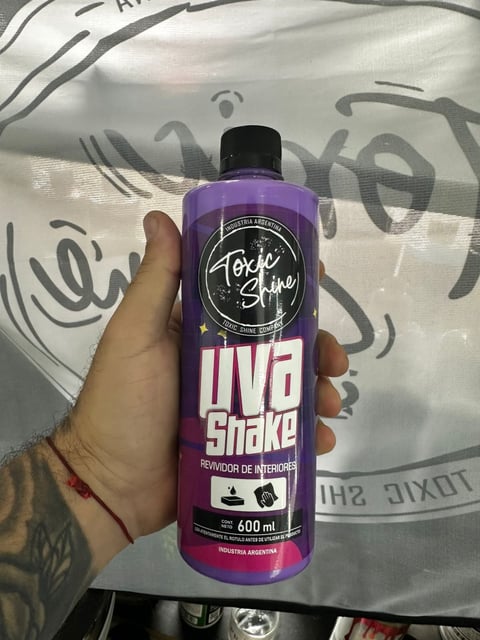 Hand holding a purple bottle of Toxic Shake interior air freshener powder, 600ml, against graffiti background