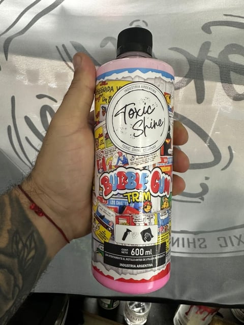 Hand holding a Toxic Shine pink spray bottle with colorful stickers and graffiti background