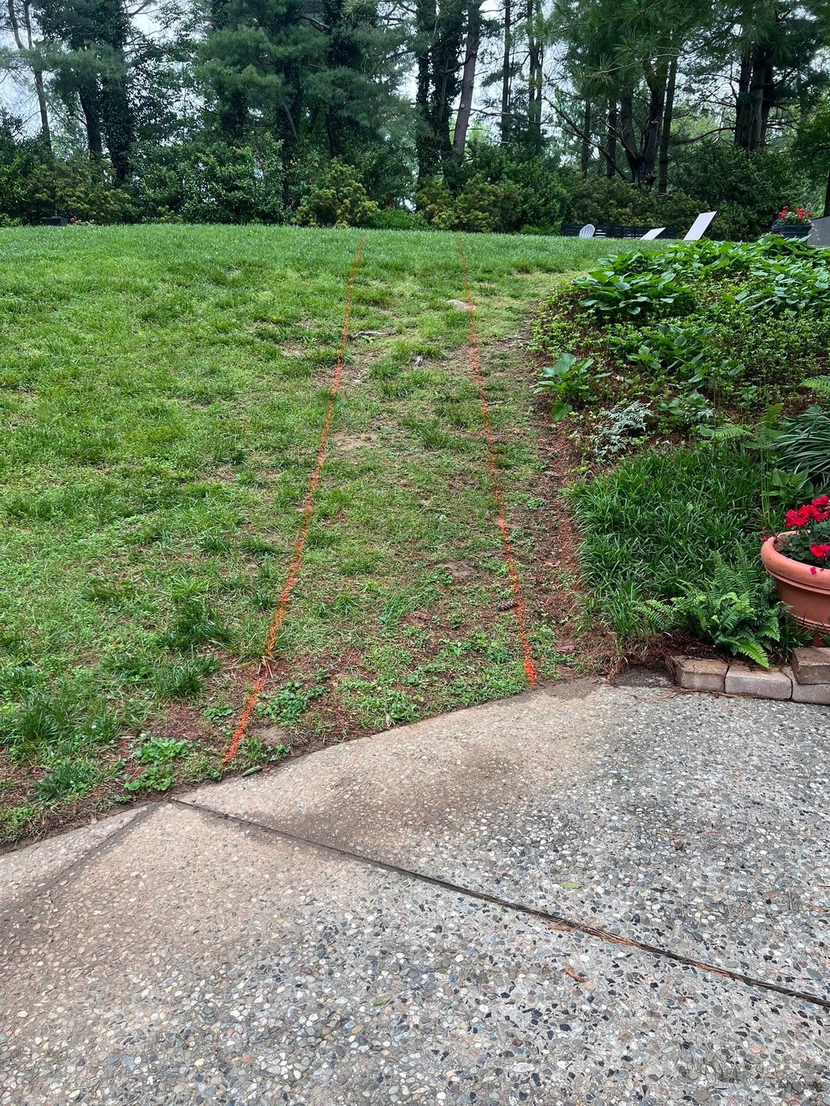 Sloped lawn with sparse grass and reddish soil before construction