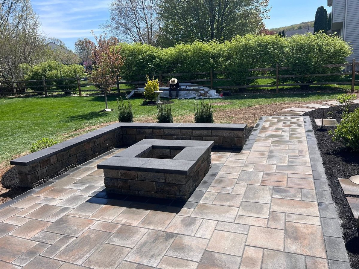 Backyard patio with stone fire pit and seating area, surrounded by manicured lawn and hedges