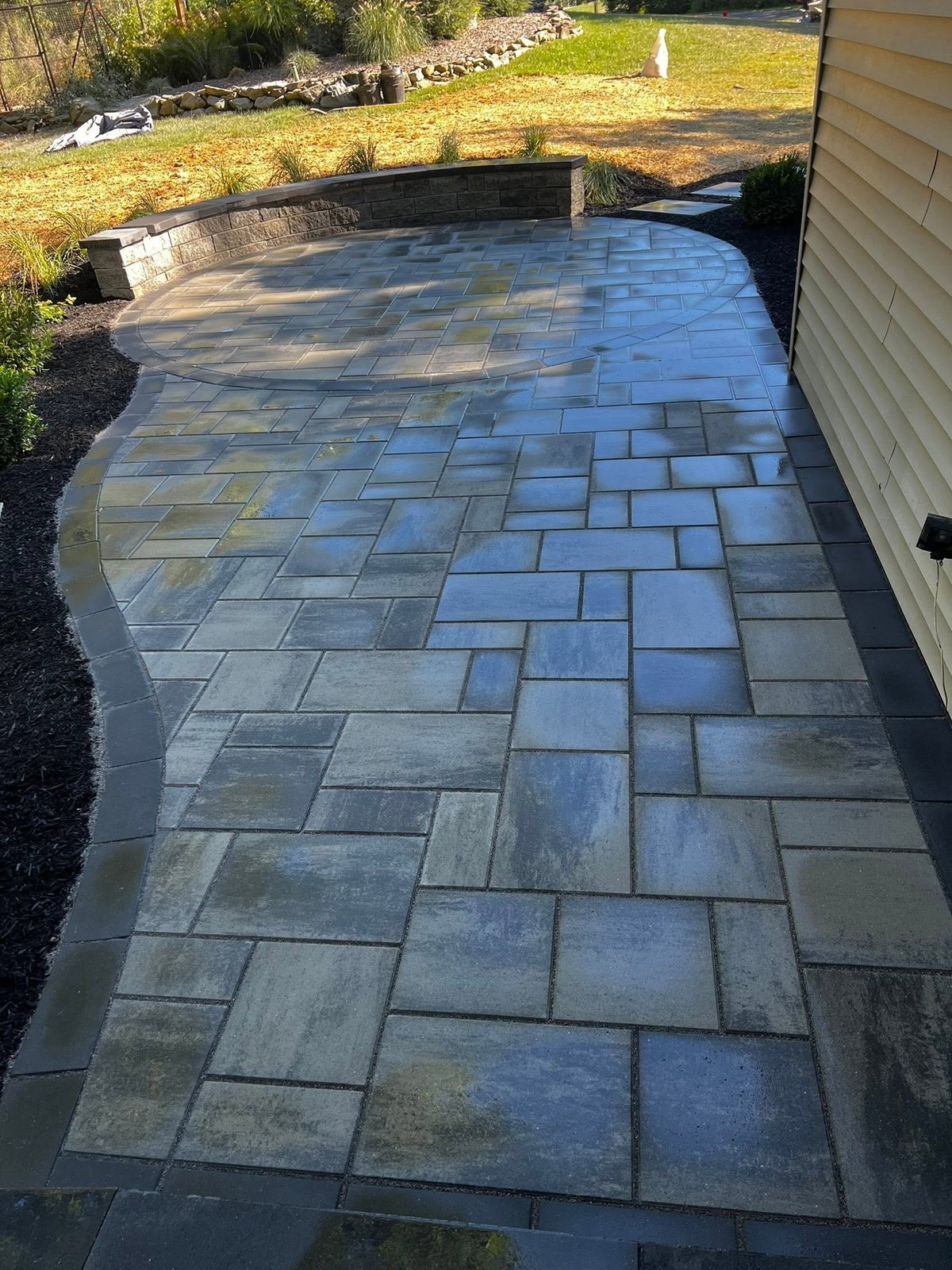 Curved patio with blue-gray stone pavers in geometric pattern, bordered by grass and landscaping