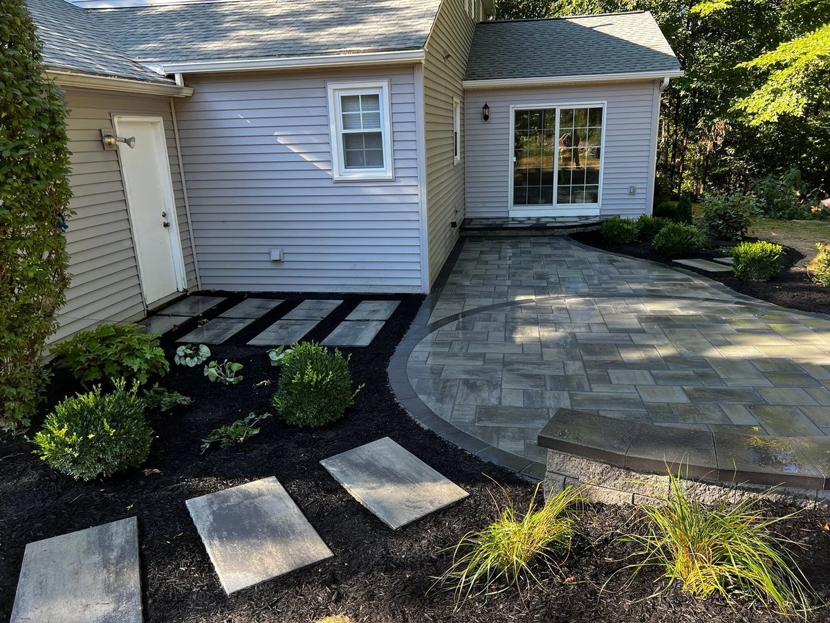 Two modern cottages with white siding connected by a paver patio and stepping stone pathway through landscaped black mulch beds with green shrubs