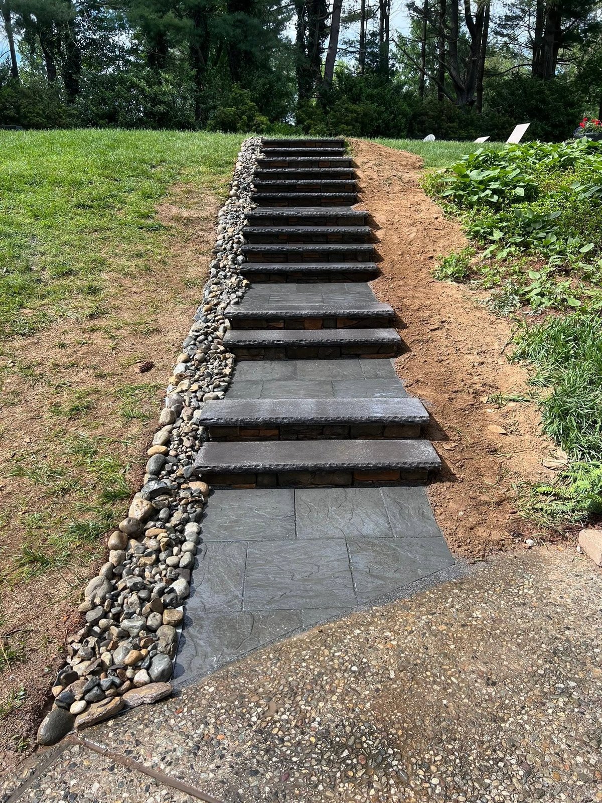 Newly built dark stone steps with river rock border through the slope
