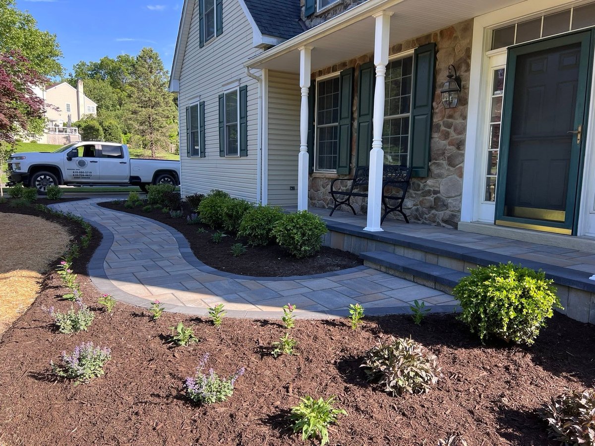 Front porch of house with curved pavers, stone accents, white columns, and newly planted landscaping shrubs