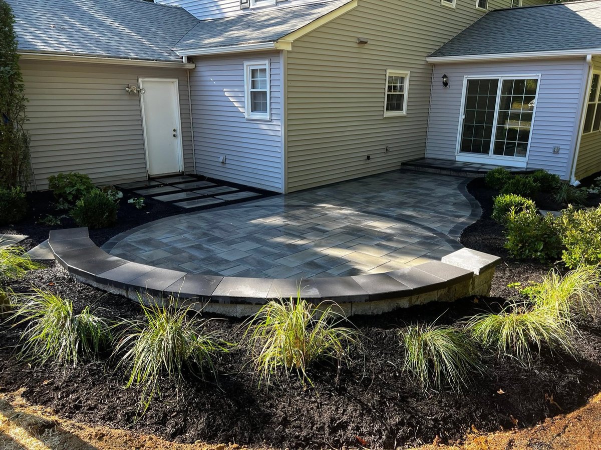 Curved stone patio behind residential home with ornamental grasses and landscaping