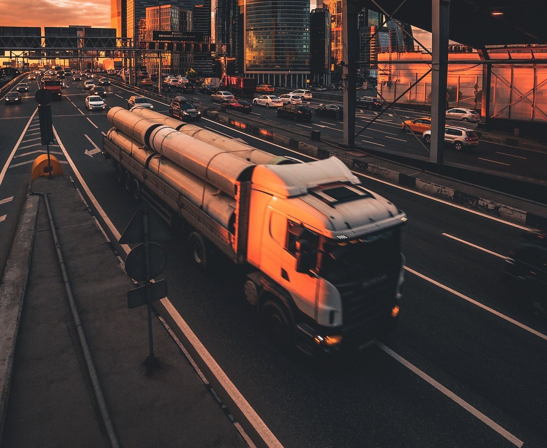 Orange and gray passenger train on urban tracks at sunset with city buildings in background
