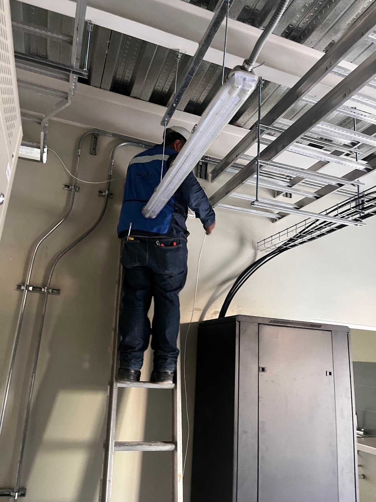 Técnico dando mantenimiento en el plafón a la infraestructura de red de una empresa, con gabinete metálico y canalizaciones