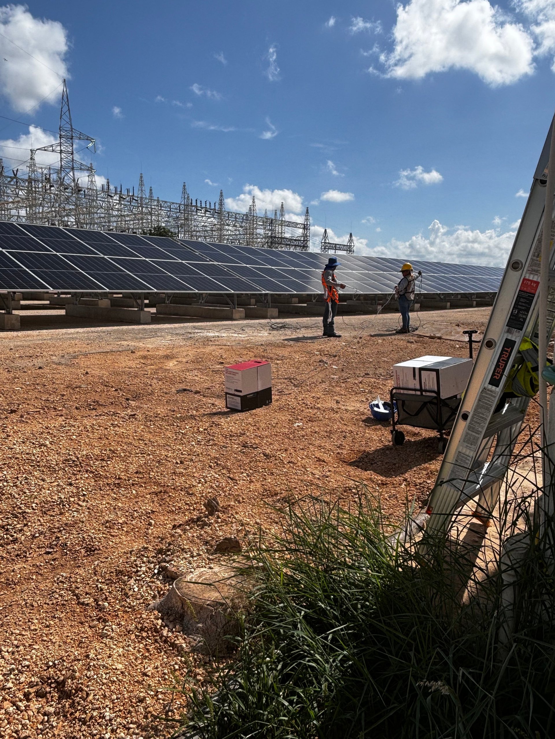 Técnicos de My Digital Manager trabajando en campo entre arreglos de paneles solares, con infraestructura de transmisión eléctrica al fondo