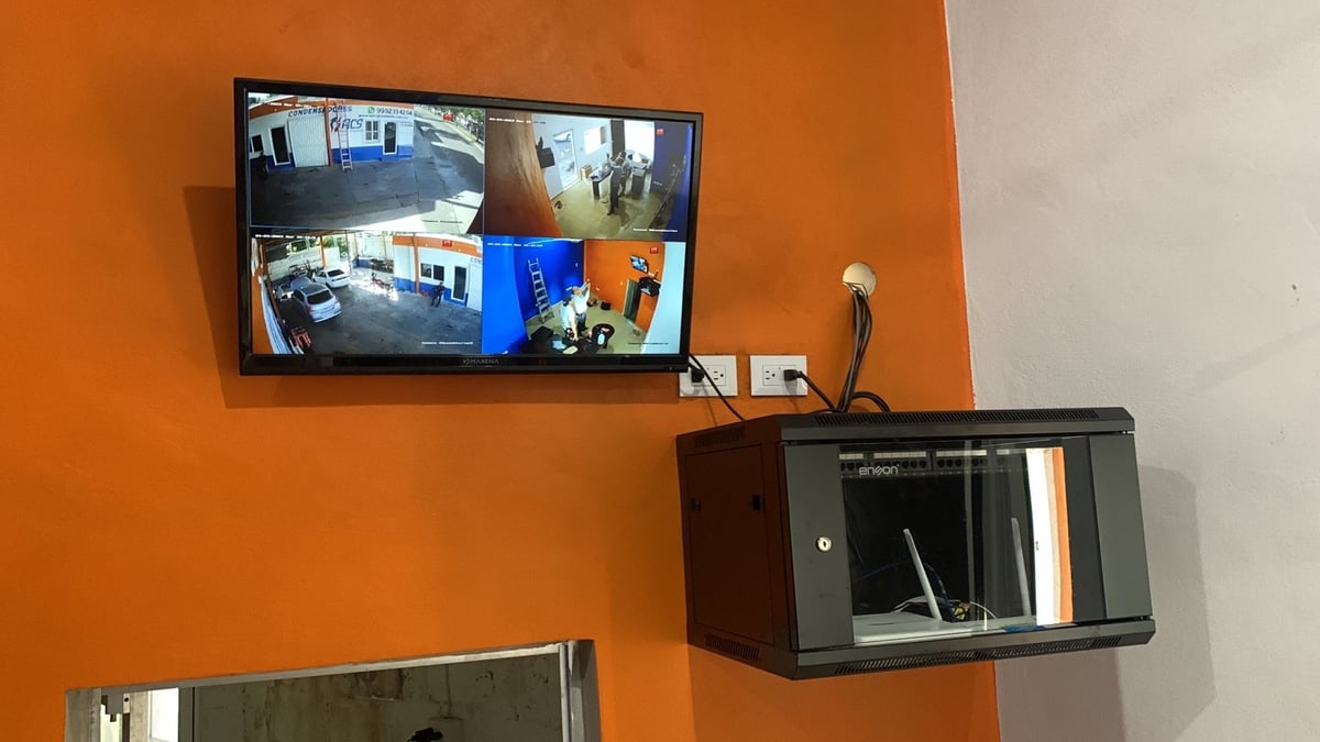 Monitor de videovigilancia instalado en sitio mostrando cuatro cámaras en vivo, junto al gabinete de comunicaciones con el equipo de red