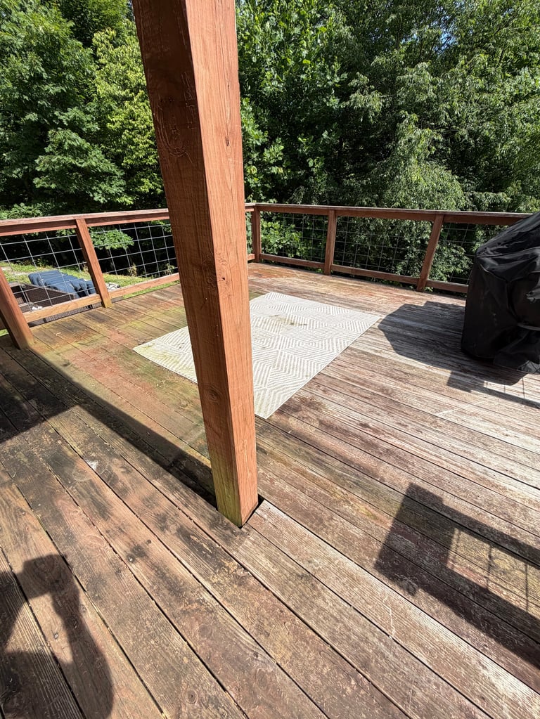 Wooden deck with metal railing overlooking forested area, featuring a central support beam and seating area.