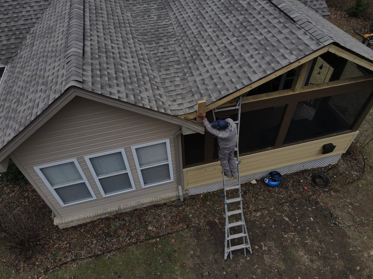 Aerial view of a house with gray roof, worker on ladder installing or repairing open roof frame above garage