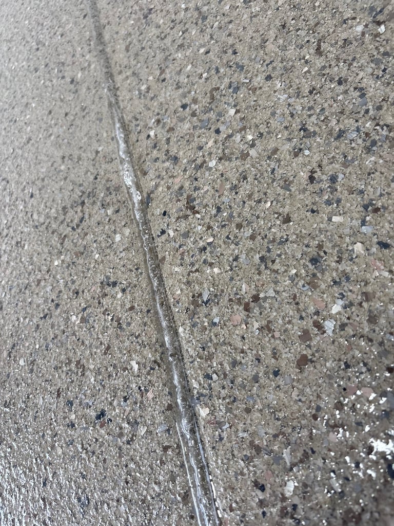 Close-up of concrete pavement with a thin crack running diagonally across textured gray surface with scattered pebbles