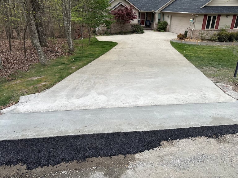 Newly installed concrete driveway leading to two-story brick home with green lawn and trees