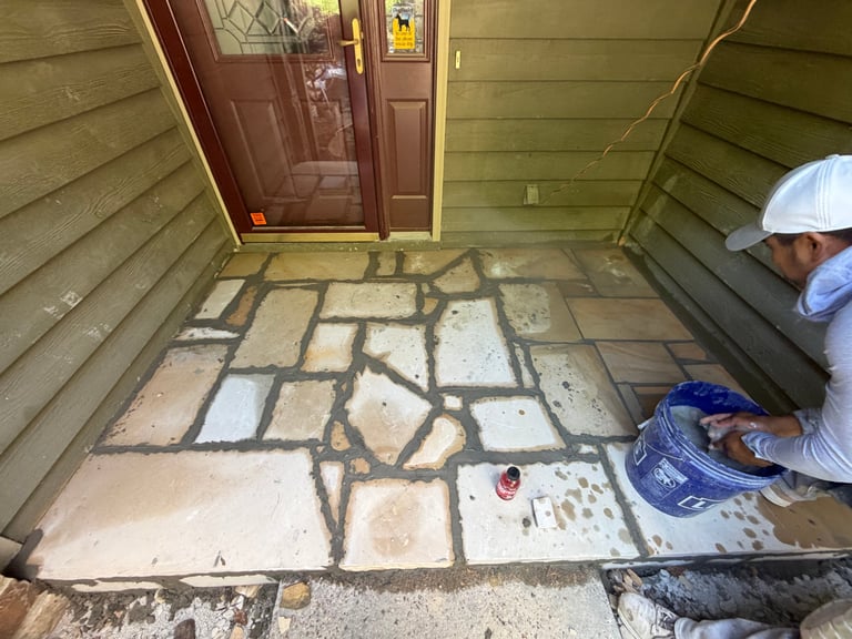 Worker applying grout between flagstone pavers on a residential porch floor during installation
