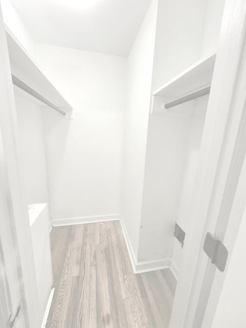 Empty walk-in closet with white walls, wood plank flooring, and metal clothing rods on both sides