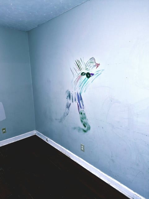 Abstract painted figure sketched onto a pale blue wall in an empty room with dark hardwood flooring