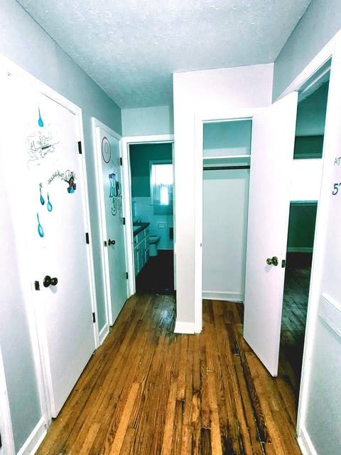 A hallway with turquoise ceiling and walls, white doors on both sides, and hardwood flooring leading to an open room.