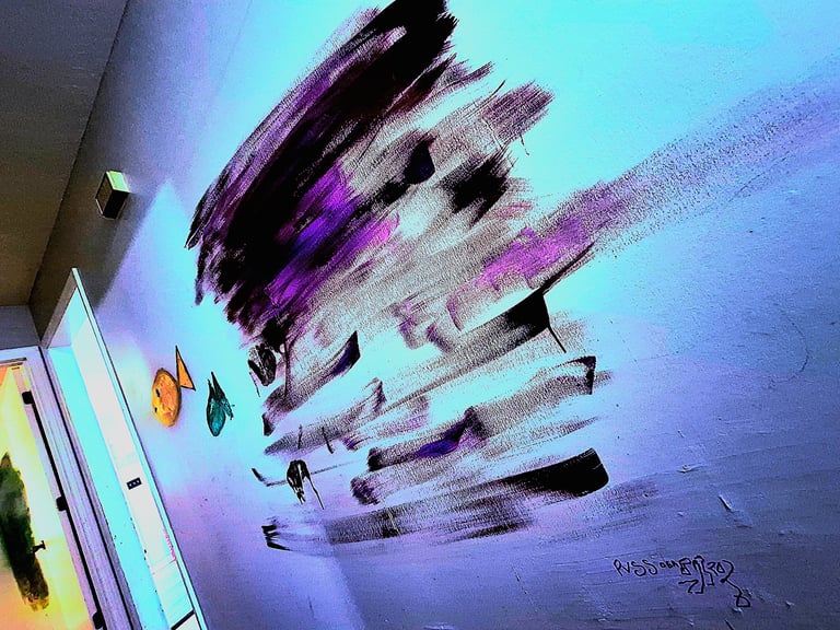 Large wall mural of purple, gray, and black brushstrokes over a teal-blue wall, with small painted fish artwork at the bottom left