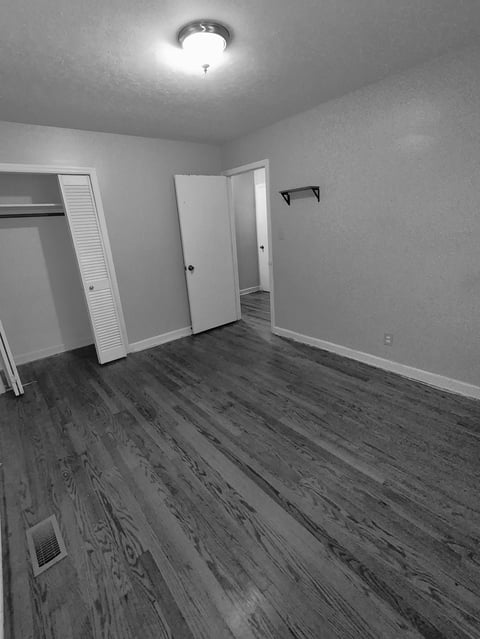 Black and white empty bedroom with hardwood floors, louvered closet doors slid open, an interior door, and a ceiling light fixture