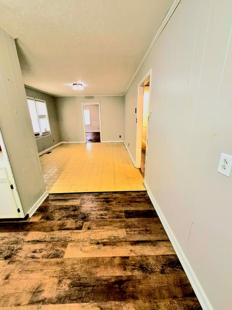 Empty apartment interior with damaged flooring, showing water damage and partial yellow subfloor replacement in progress
