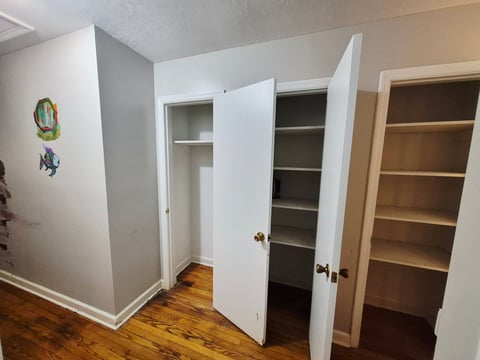 Interior room with open closet doors revealing built-in shelving on the right, hardwood floors, and small fish artwork on the left wall