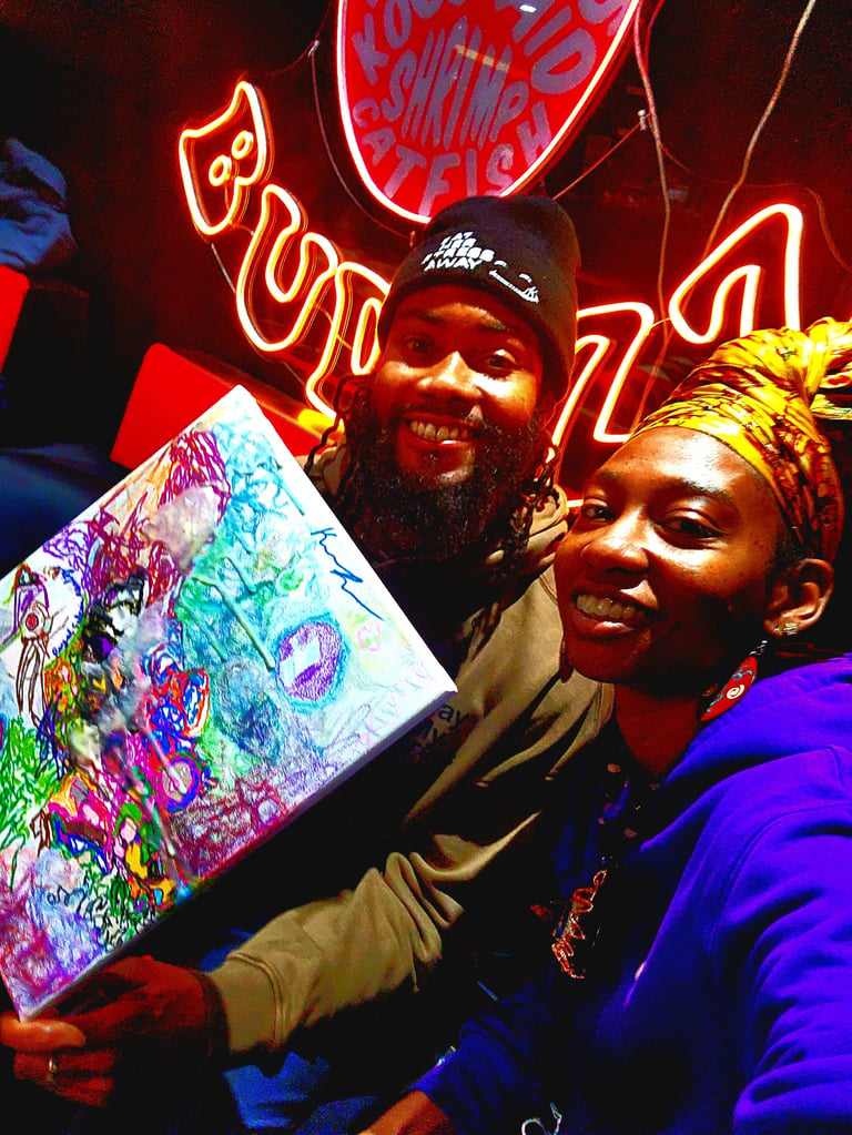 Two people smiling while holding a colorful artwork in front of neon signs at night