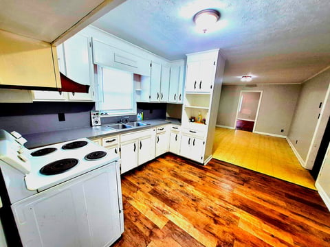 Spacious kitchen with white cabinets, electric stove, and warm wood flooring throughout the room.