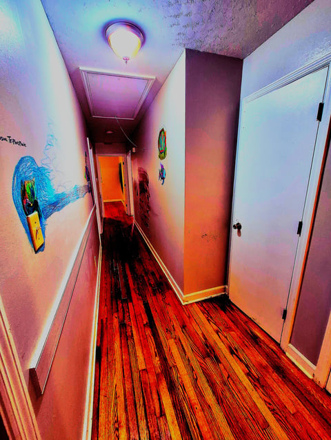 Narrow hallway with vibrant neon lighting in pink, purple, and orange hues, hardwood floors, and colorful mural artwork on the walls