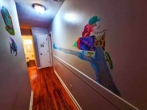 Hallway with tropical fish murals on the left wall, an abstract tree mural on the right, hardwood floors, and a white door numbered 55