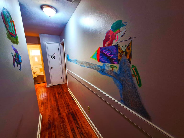 Hallway with tropical fish murals on the left wall, an abstract tree mural on the right, hardwood floors, and a white door numbered 55