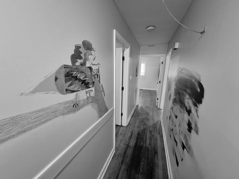 Black and white hallway view with hand-drawn murals on both walls, hardwood floors, and a doorway at the end