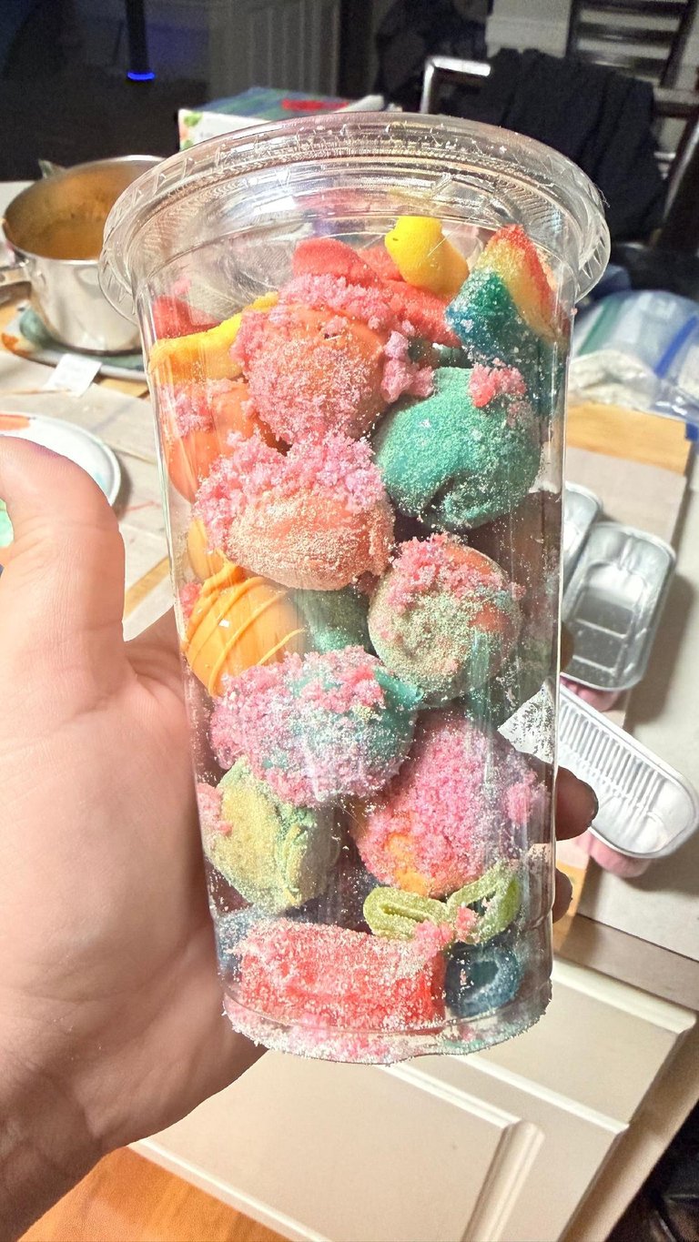 Hand holding a clear cup filled with colorful sour gummy candies coated in sugar in pink, green, yellow, and red colors