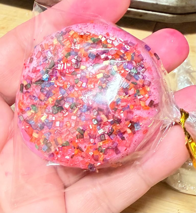 Hand holding a clear plastic ball filled with pink liquid and colorful confetti glitter