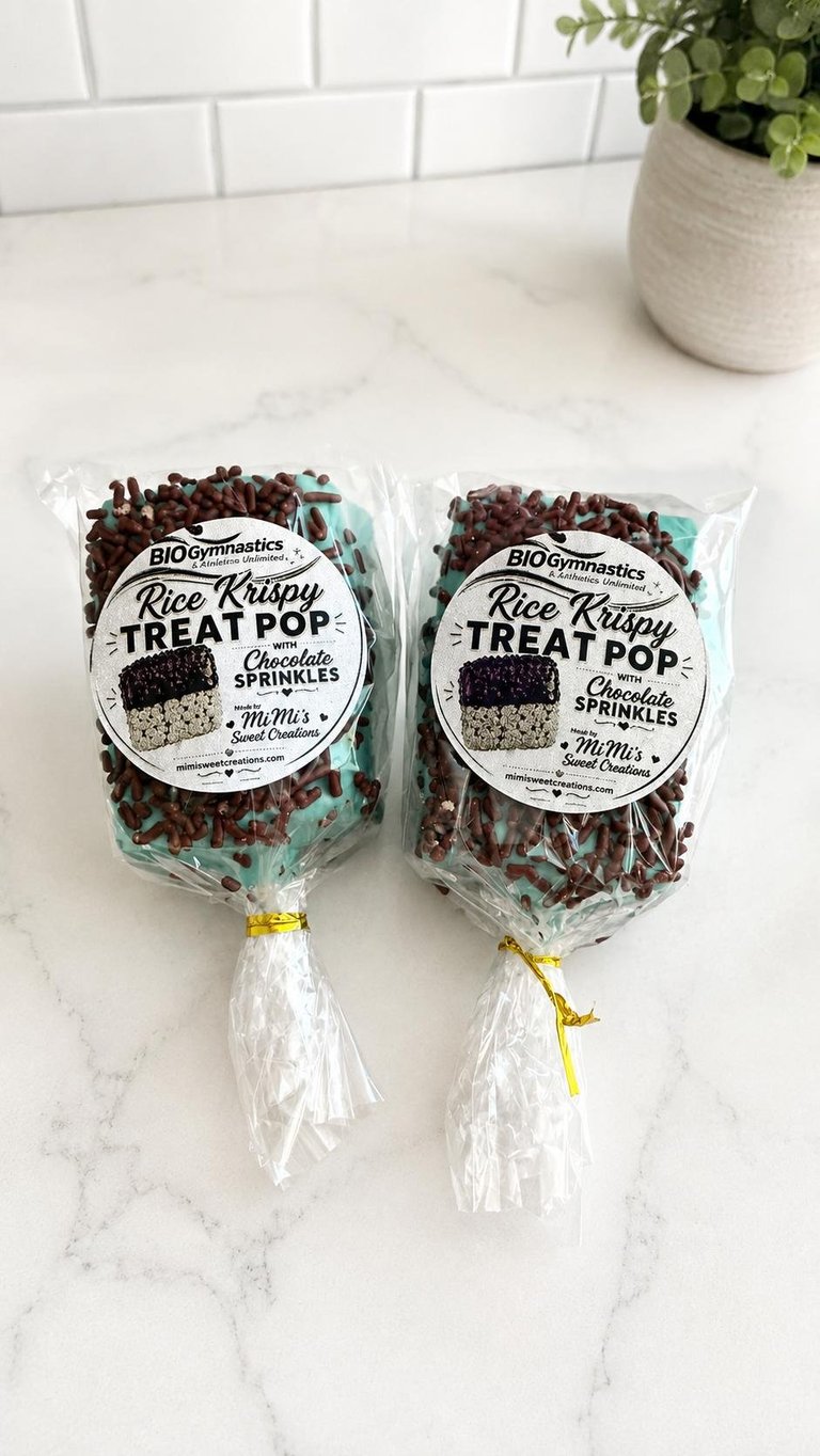 Two packages of BIOgymnastics Rice Krispie Treat Pop with chocolate sprinkles on a marble countertop next to a potted plant