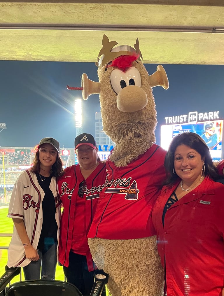 Three people posing with the Atlanta Braves mascot at Truist Park baseball stadium at night