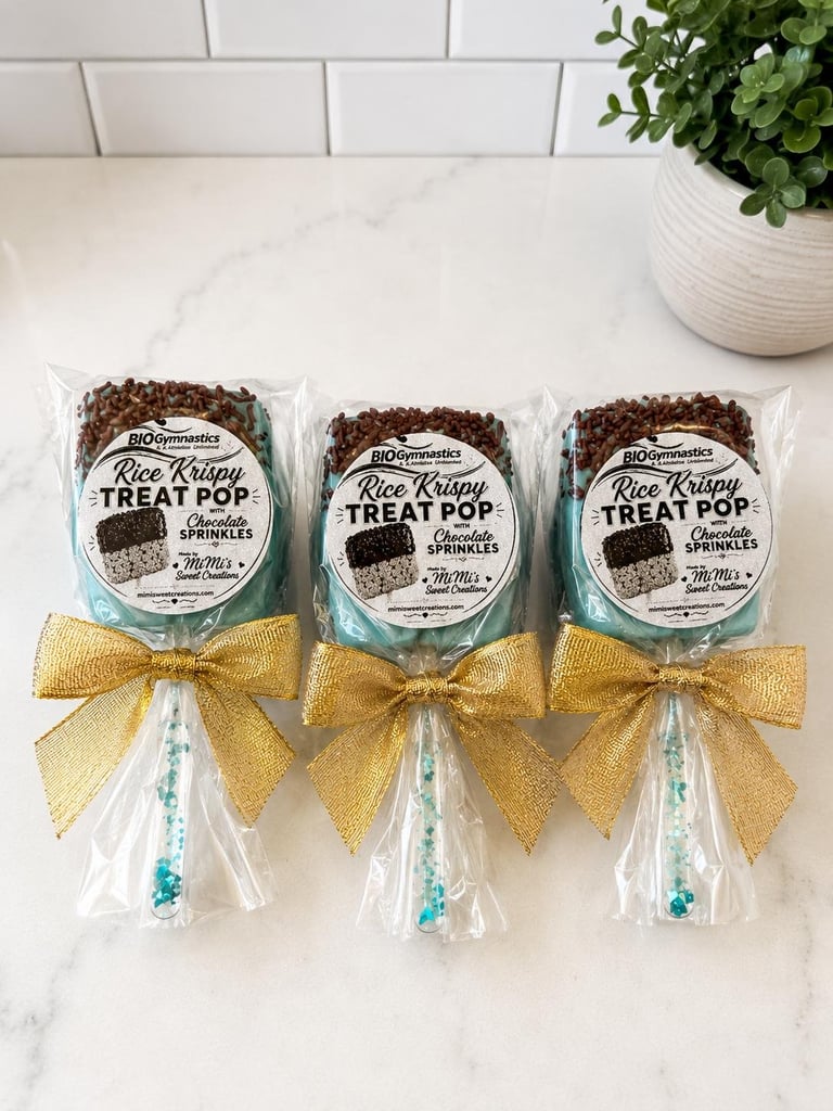 Three rice krispy treat pops with gold bows and sprinkles arranged on a marble surface with white subway tile and potted plant in background